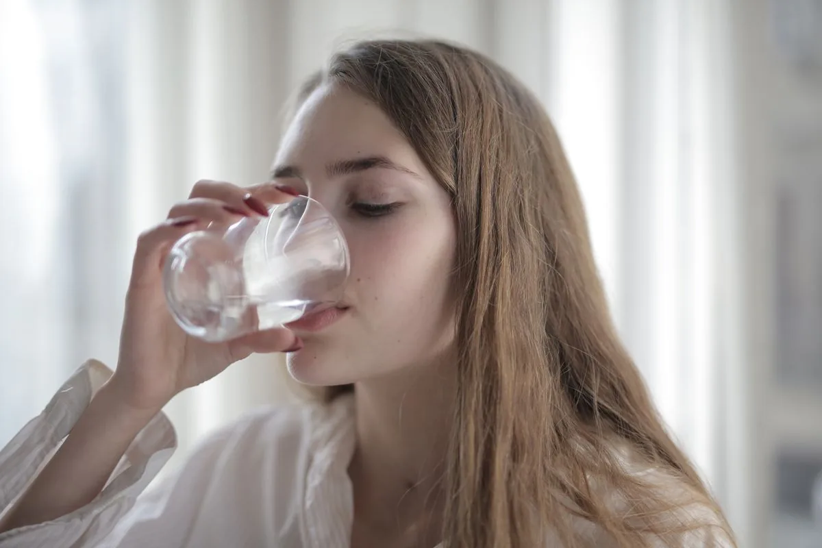 Dona bevent un got d'aigua a contrallum, el gest més eficaç per prevenir la cistitis i les infeccions d'orina a l'estiu
