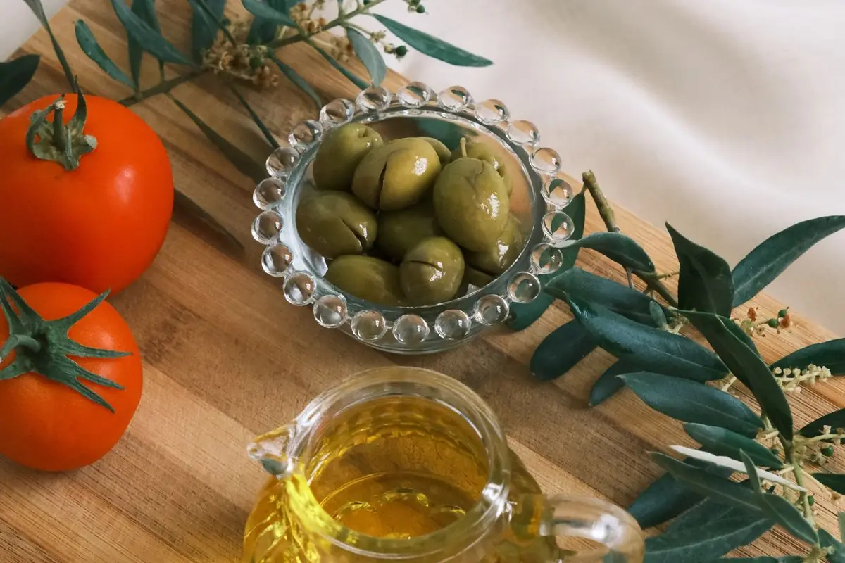 Oli d'oliva verge, olives i tomàquets sobre una taula de fusta, la base de la dieta mediterrània per baixar el colesterol