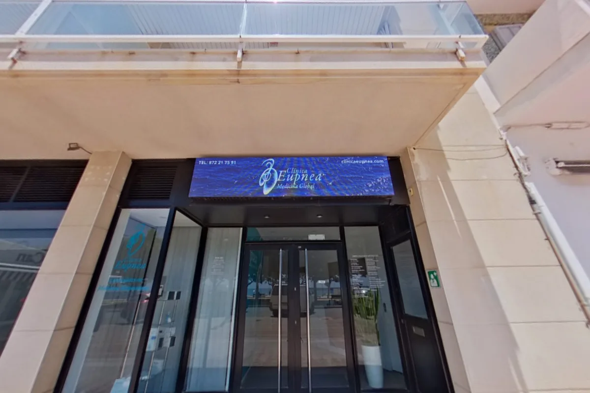 Entrance of Clínica Eupnea at Passeig del Mar, 41, Palamós, with the clinic's illuminated sign