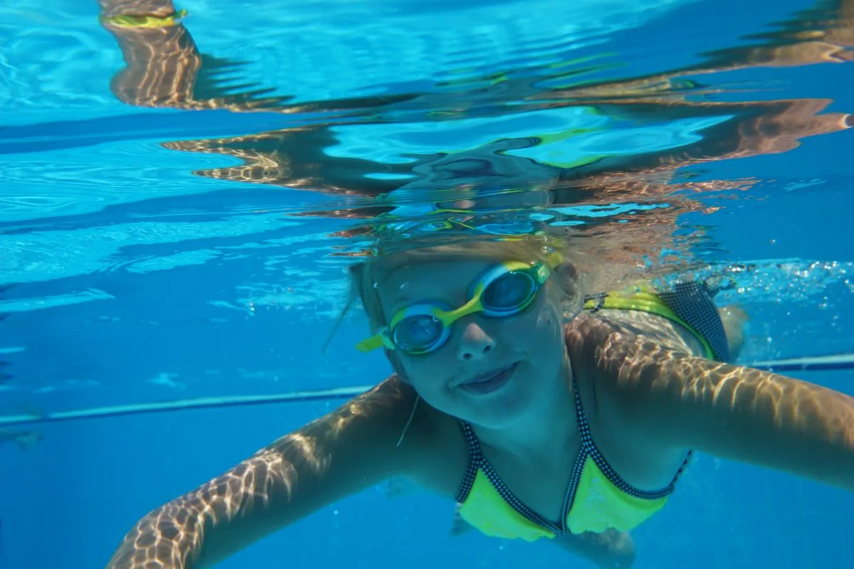 Nen nedant sota l'aigua en una piscina, situació que afavoreix l'otitis del nedador o otitis externa