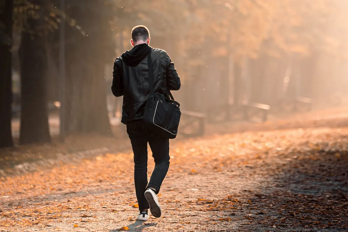 Man walking along a leaf-covered path in the light of an autumn morning: getting out into natural daylight early in the day is one of the measures that help with seasonal depression