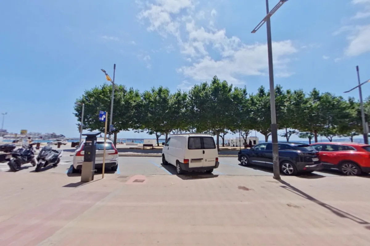 Passeig del Mar de Palamós vist des de la porta de Clínica Eupnea, amb cotxes aparcats, els arbres del passeig i el mar al fons