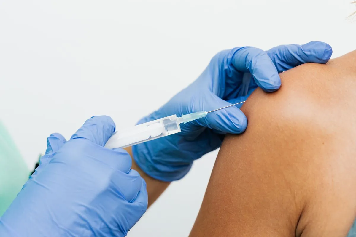 Gros plan d'un vaccin injecté dans le bras avec des gants, la voie intramusculaire habituelle du vaccin antigrippal
