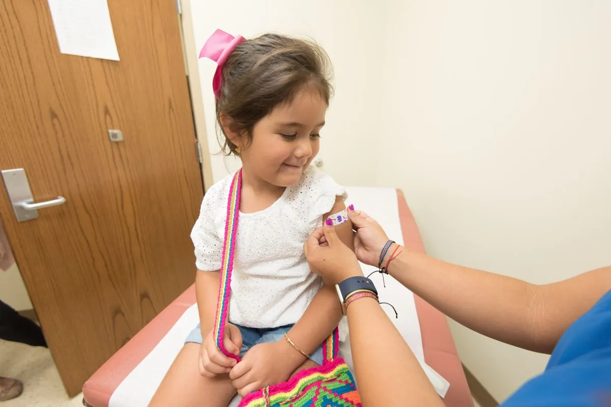 Petite fille souriante pendant qu'une professionnelle de santé lui pose un pansement sur le bras après le vaccin contre la grippe au cabinet