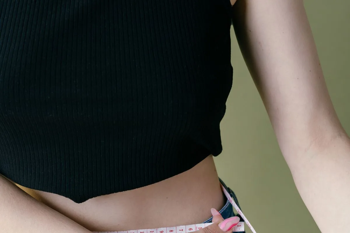 Dona amb top negre mesurant-se la cintura, la zona abdominal que es tonifica amb ProDefine Body Sculpt